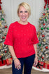 Woman wearing a red sweater with rhinestone in front of Christmas trees.