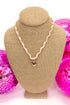 necklace with light pink ribbon and chain surrounding ribbon with a small heart pendant