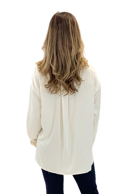 Back view of woman wearing Cream Oversized Satin Shirt with jeans against tan studio background.