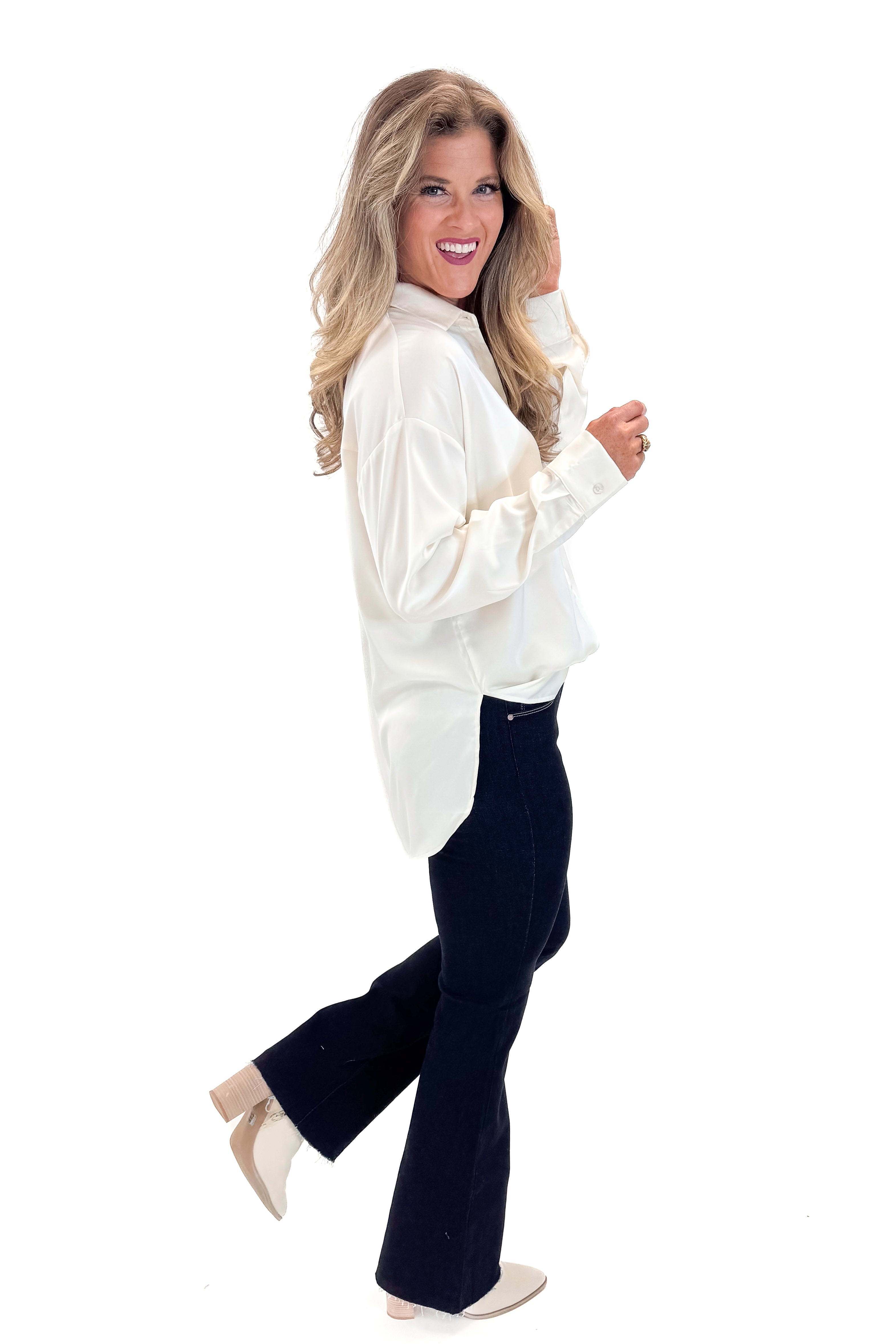 Side view of woman wearing Cream Oversized Satin Shirt with jeans against tan studio background.