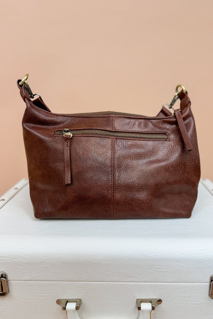 Brown leather handbag on a white surface with a beige background