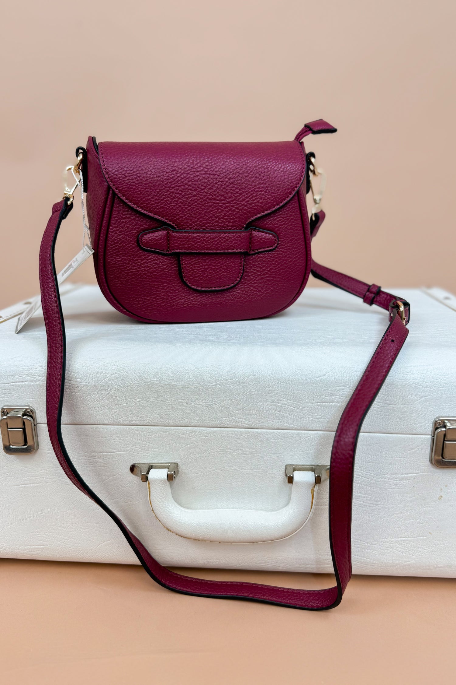Magenta handbag with a strap on a white suitcase against a beige background