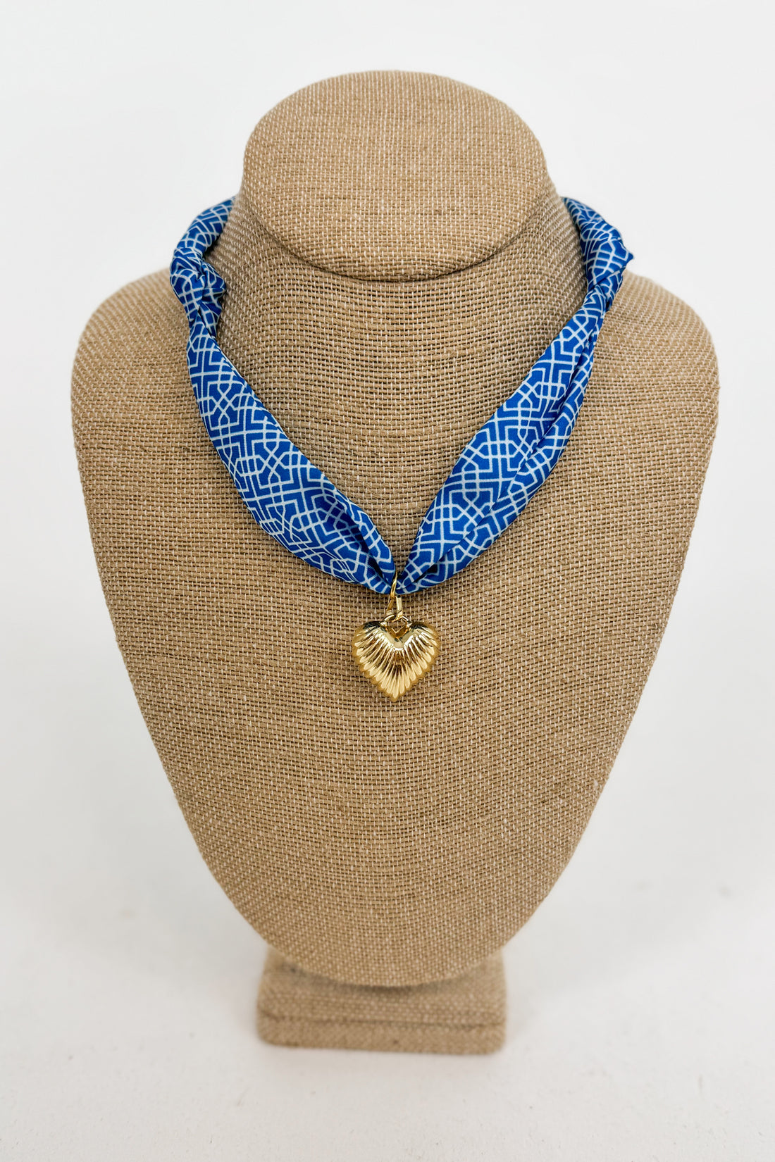 Blue patterned necklace with a gold heart pendant on a brown bust