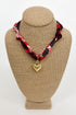Necklace with a red and black patterned strap and gold heart pendant on a beige bust.