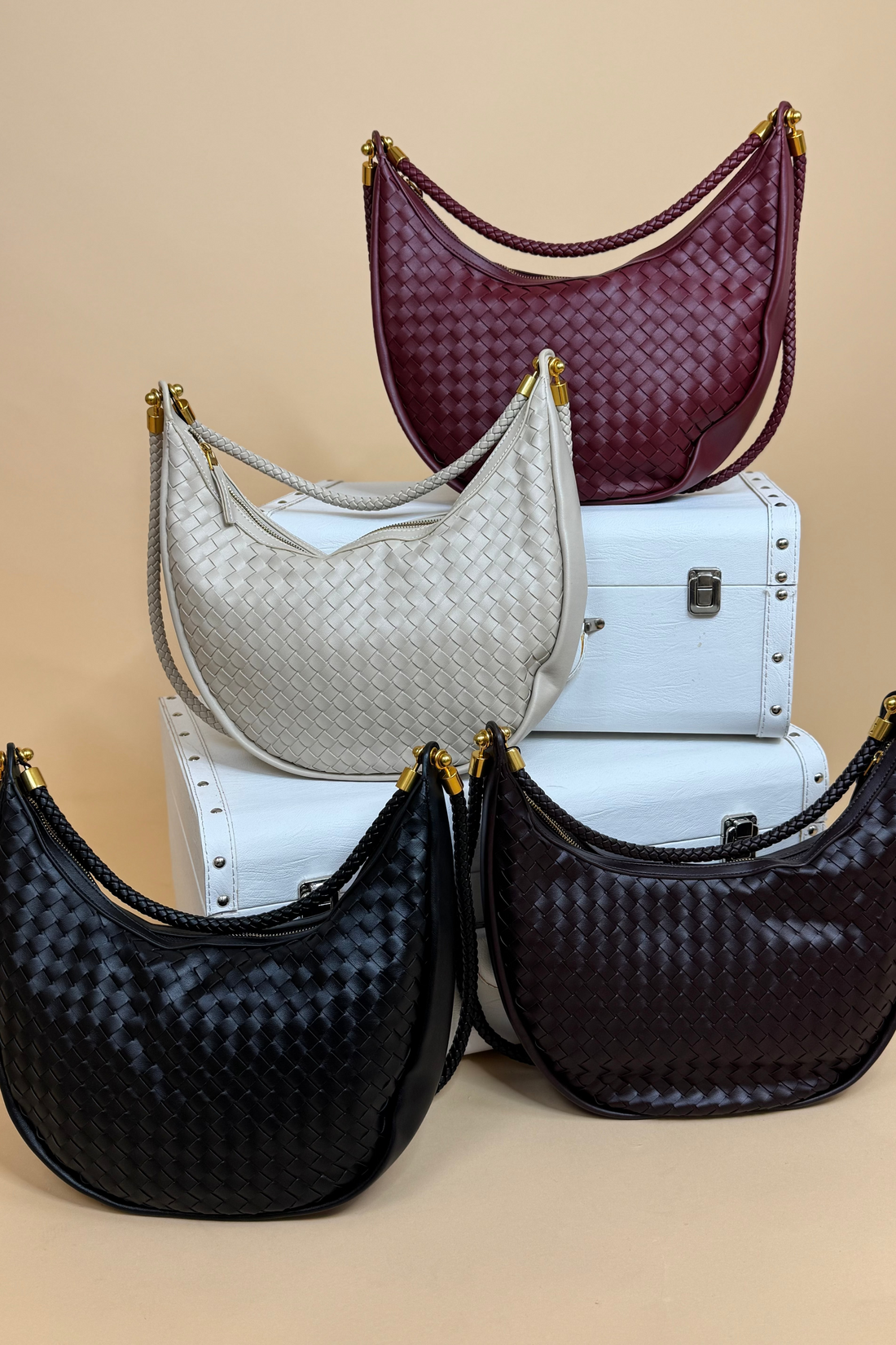 Four handbags in black, white, and burgundy on a beige background
