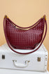 Maroon woven handbag with gold accents on a white suitcase against a beige background