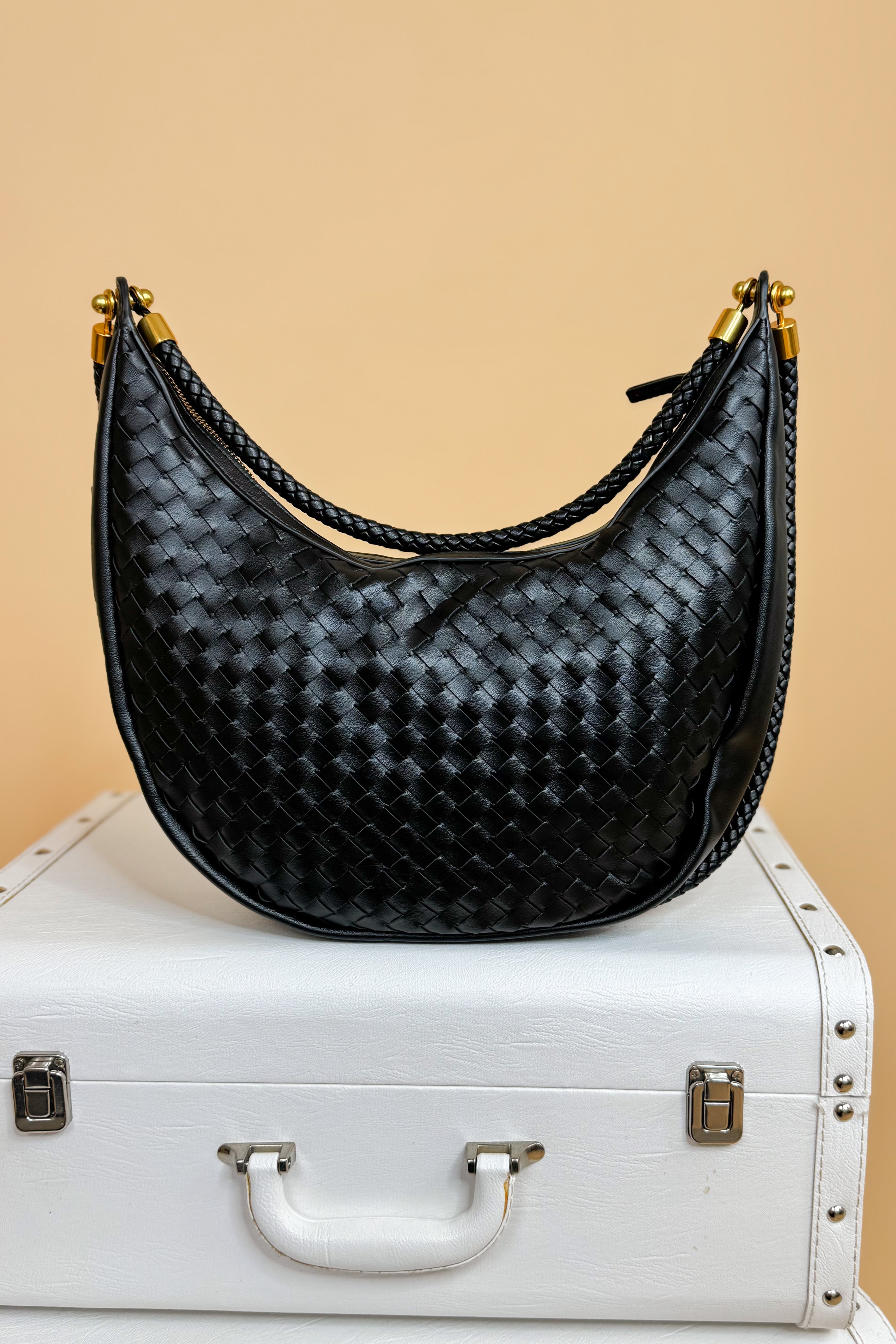 Black woven handbag on a white suitcase with a beige background