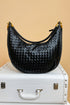 Black woven handbag on a white suitcase with a beige background