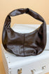 Brown leather handbag on a white surface with a beige background