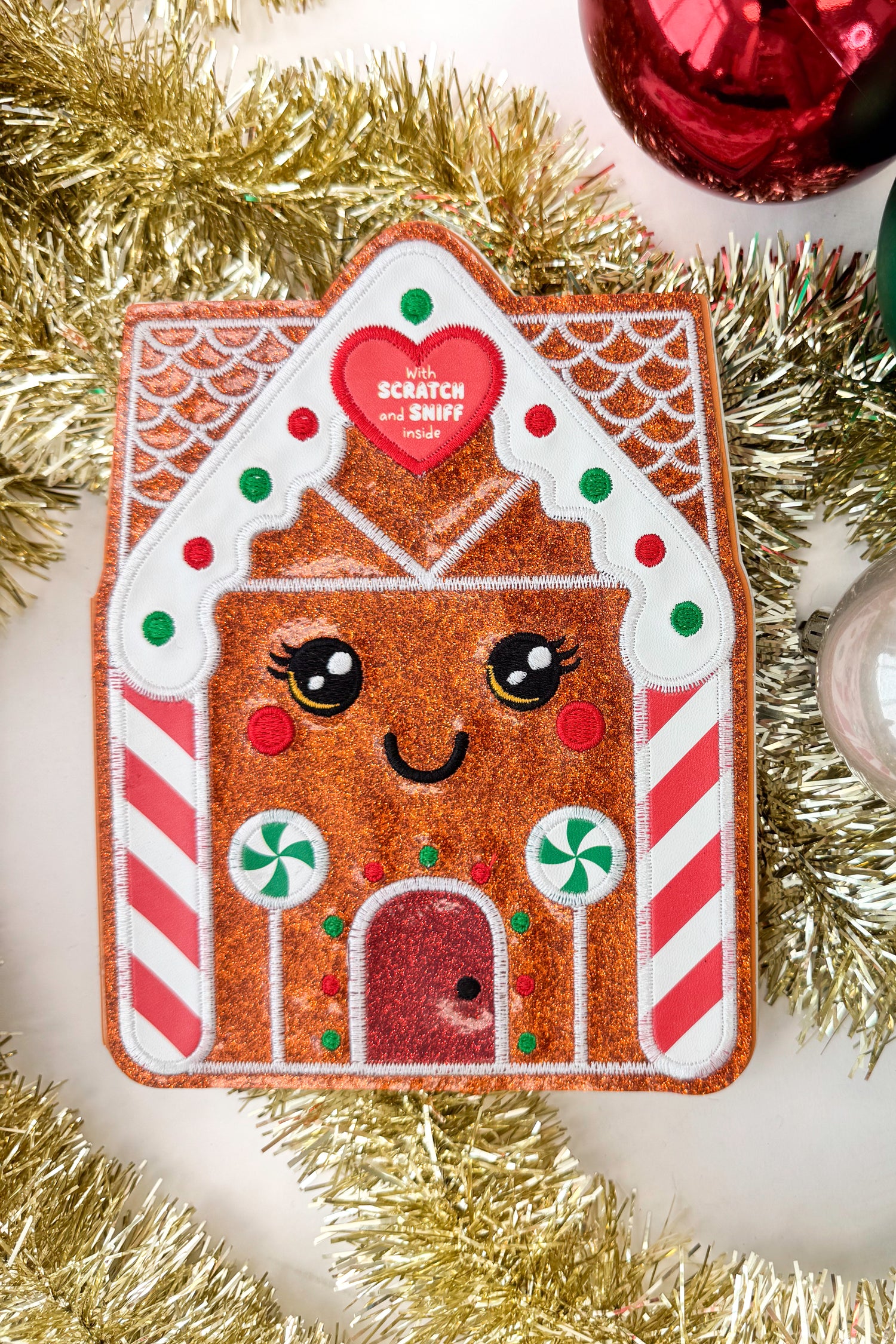 Gingerbread house-shaped scratch and sniff book with a heart label on a white background