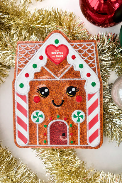 Gingerbread house-shaped scratch and sniff book with a heart label on a white background