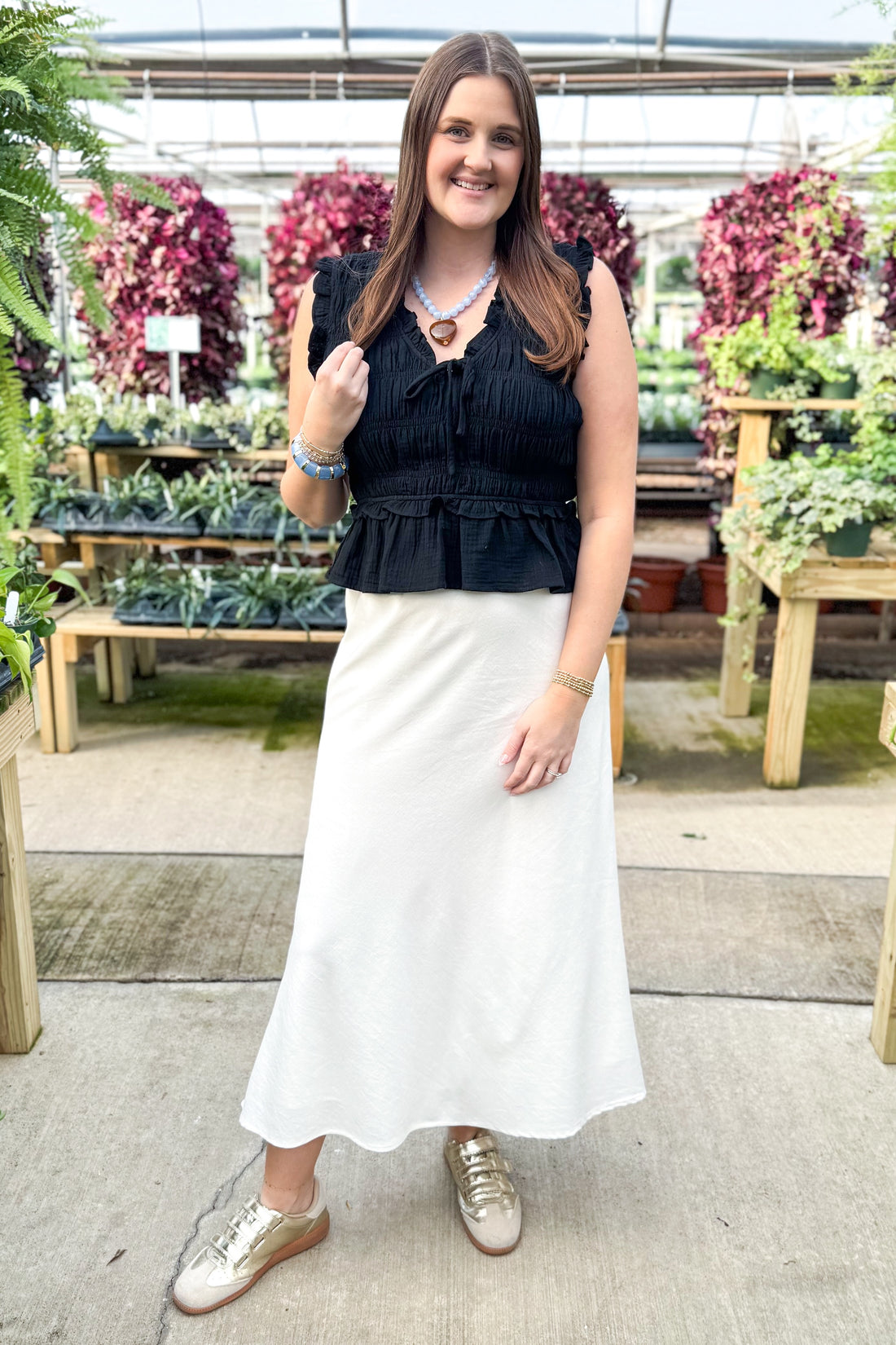 Front view of woman wearing Black Smocked Peplum Tank with skirt at a garden center.