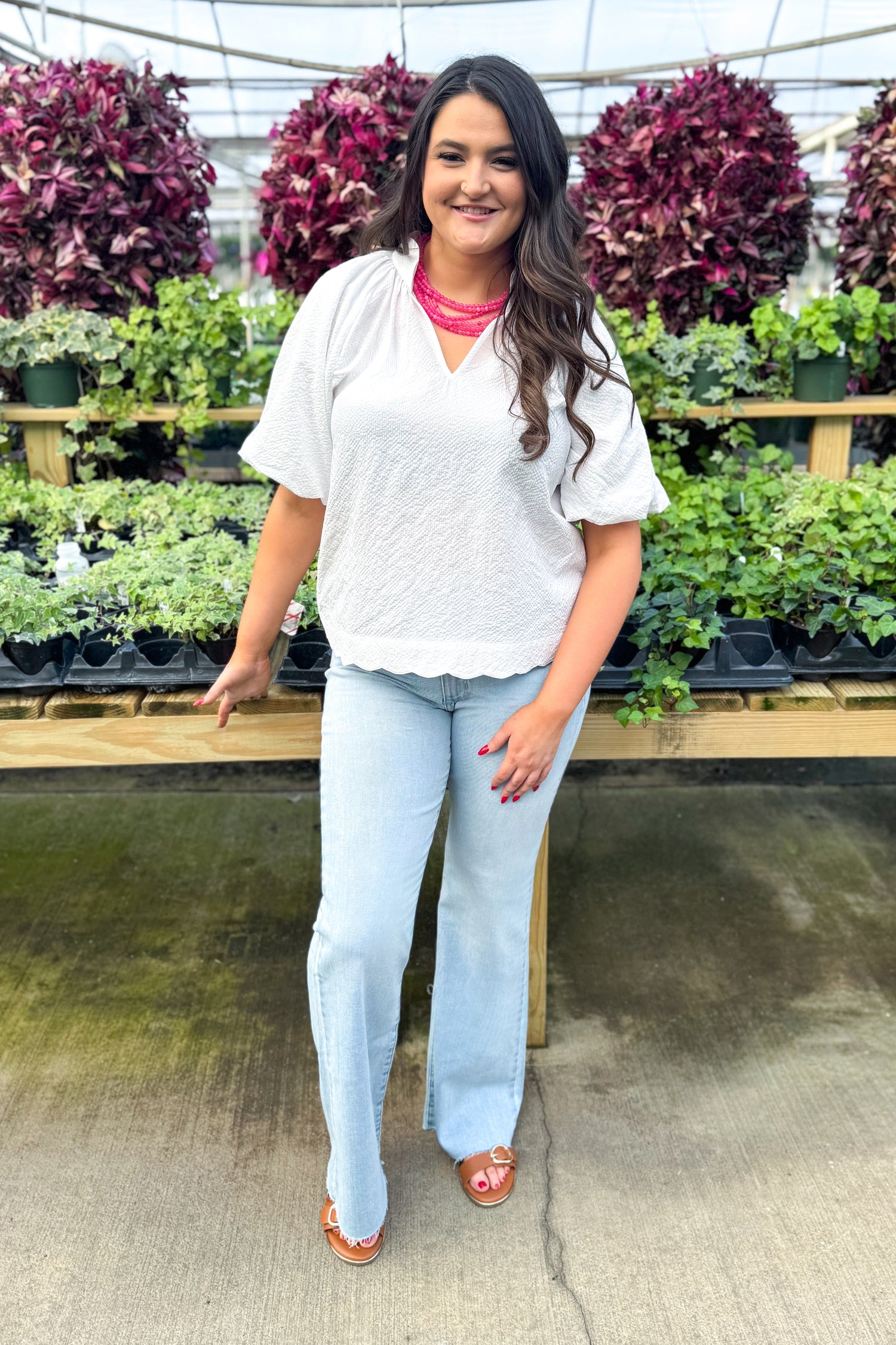 Front view of woman wearing White Scallop Detail V-neck Top with jeans at a garden center