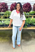 Front view of woman wearing White Scallop Detail V-neck Top with jeans at a garden center