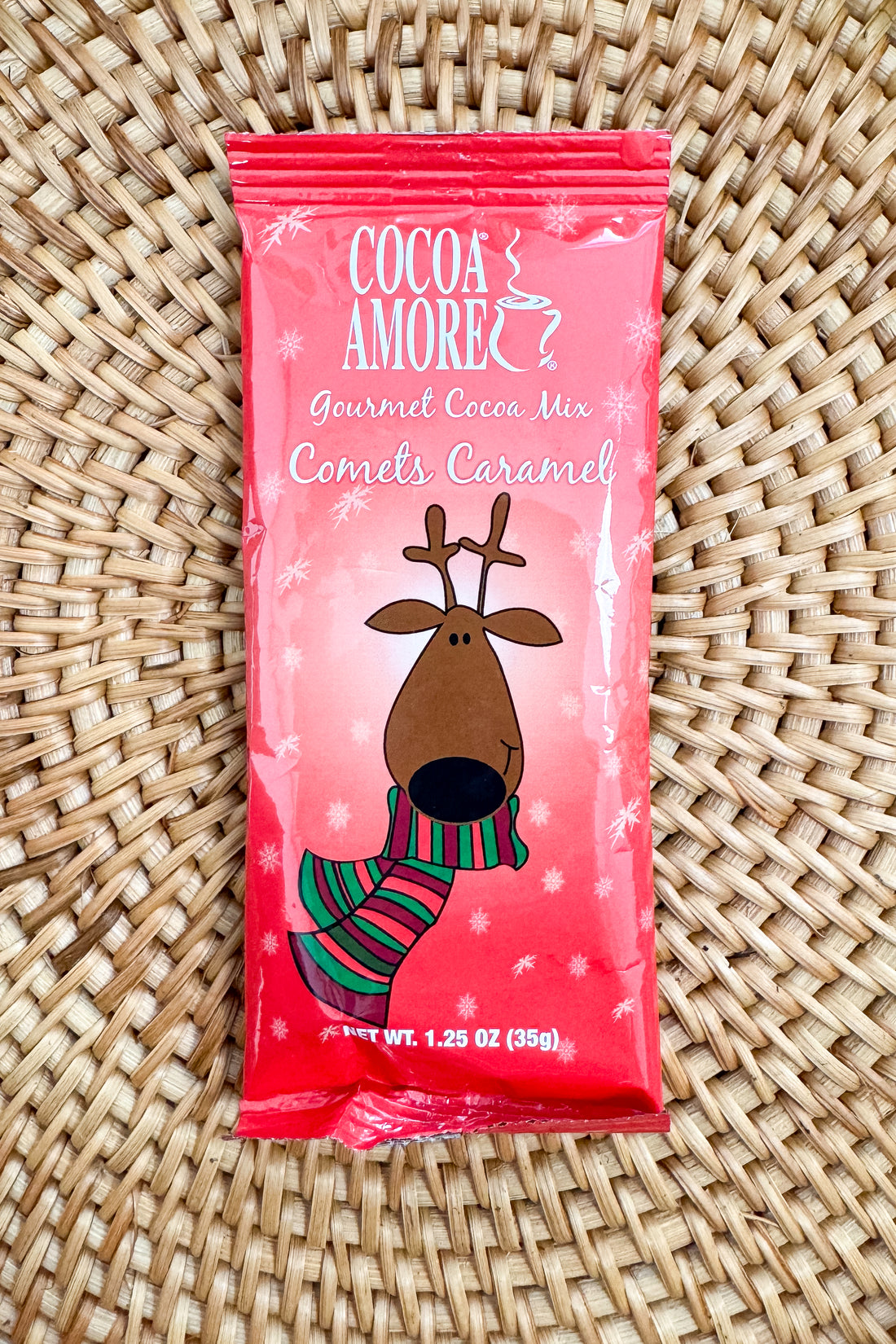 Red package of Cocoa Amore Gourmet Cocoa Mix with a reindeer design on a patterned background