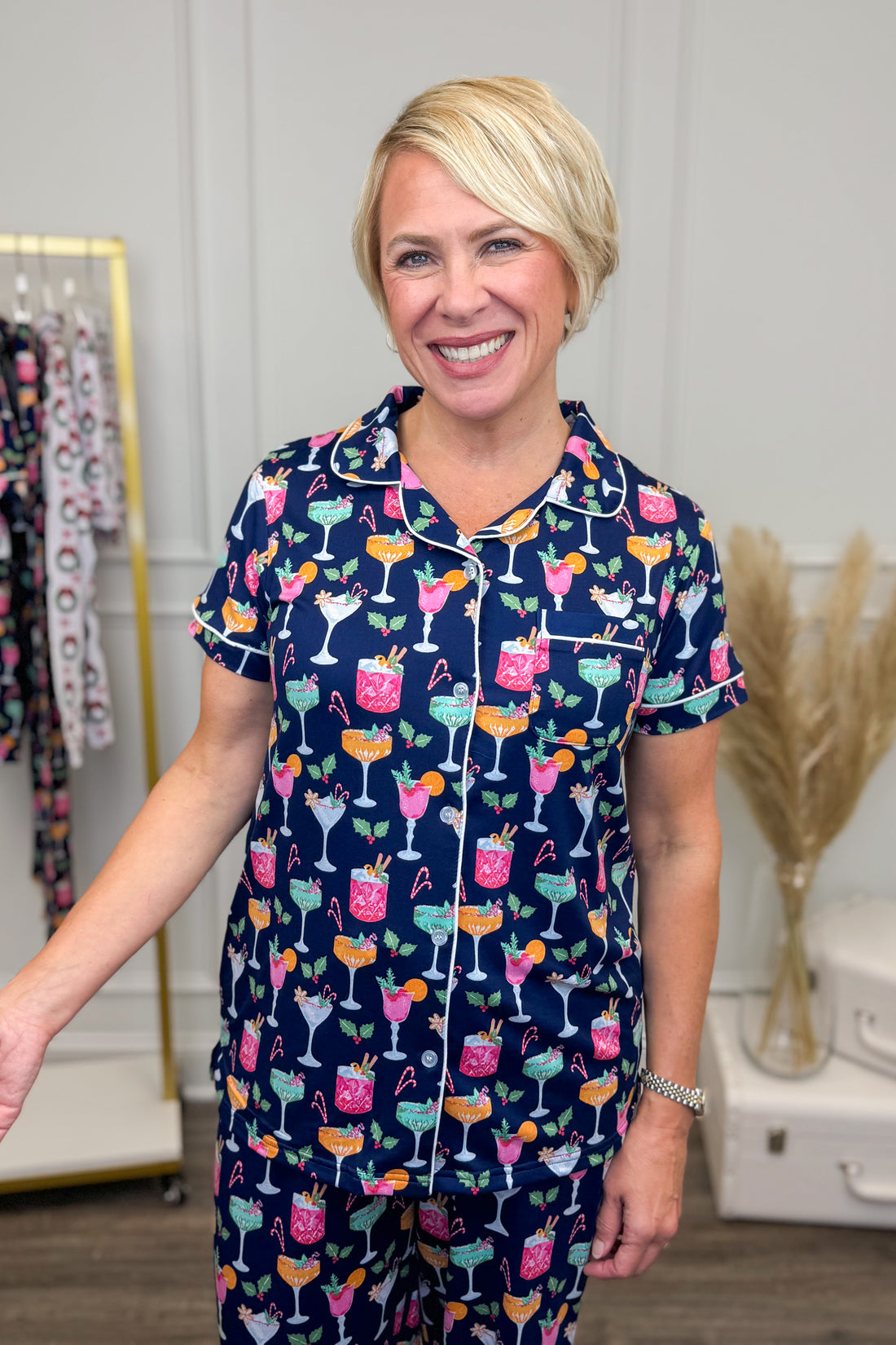 Woman wearing a navy pajama set with colorful cocktail pattern in a room.
