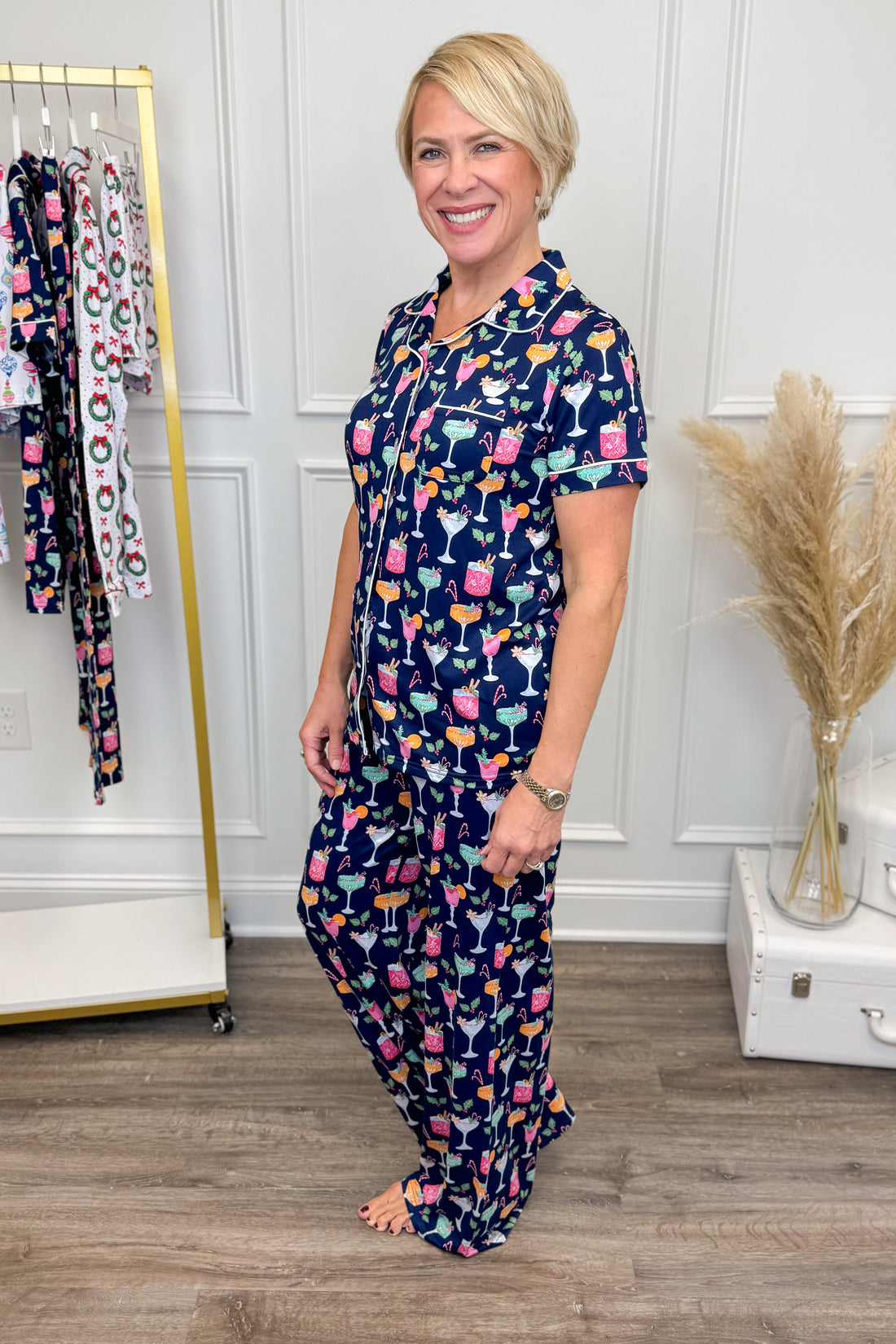 Woman wearing a navy pajama set with colorful patterns in a room with a rack of pajamas and decorative items.