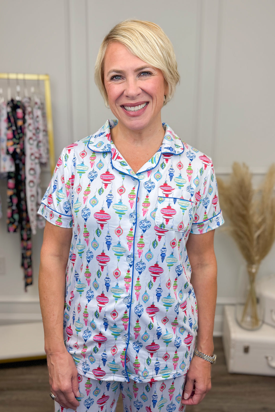 Woman wearing a colorful pajama set with a pattern of Christmas ornaments in a room.