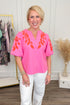 Woman wearing Pink & Orange Floral Embroidered V-Neck Top with jeans with clothes & decor in the background.