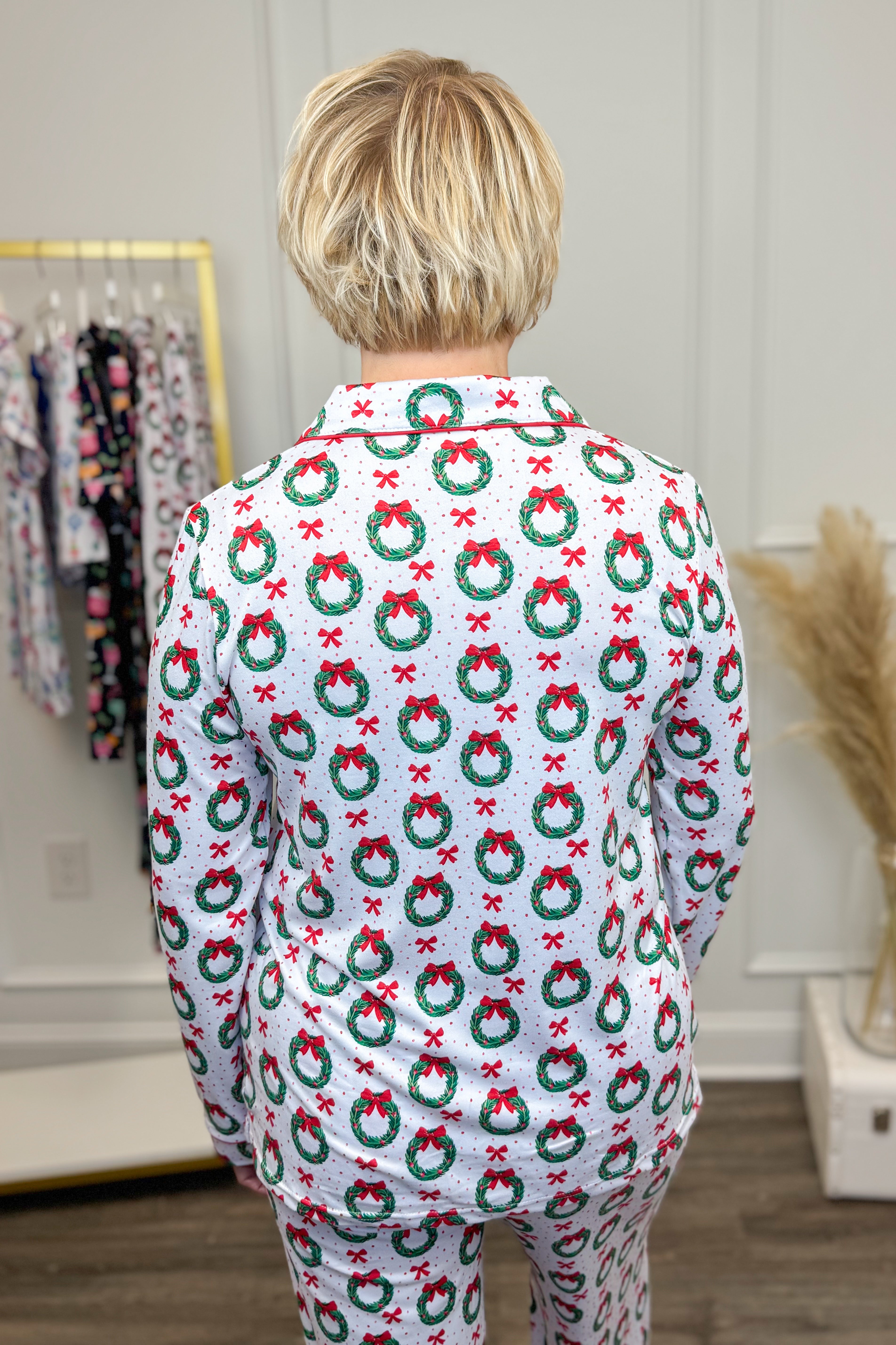 Woman wearing a patterned pajama set in a room with a rack of clothes and decorative elements.