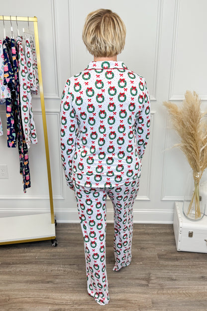 Person wearing a festive pajama set with wreath pattern in a room setting.