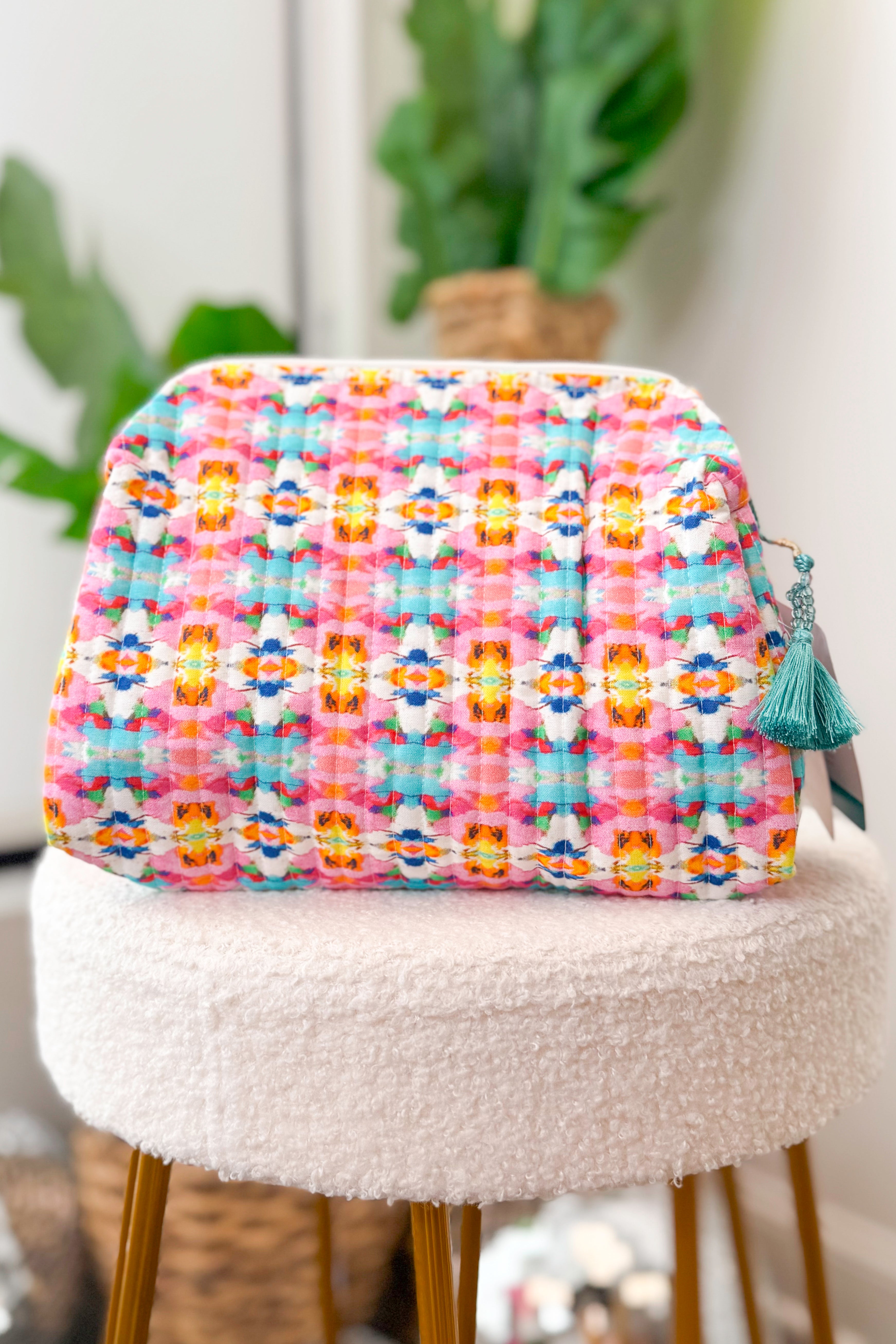 Multicolored floral-patterned pouch on a white stool with plants in the background