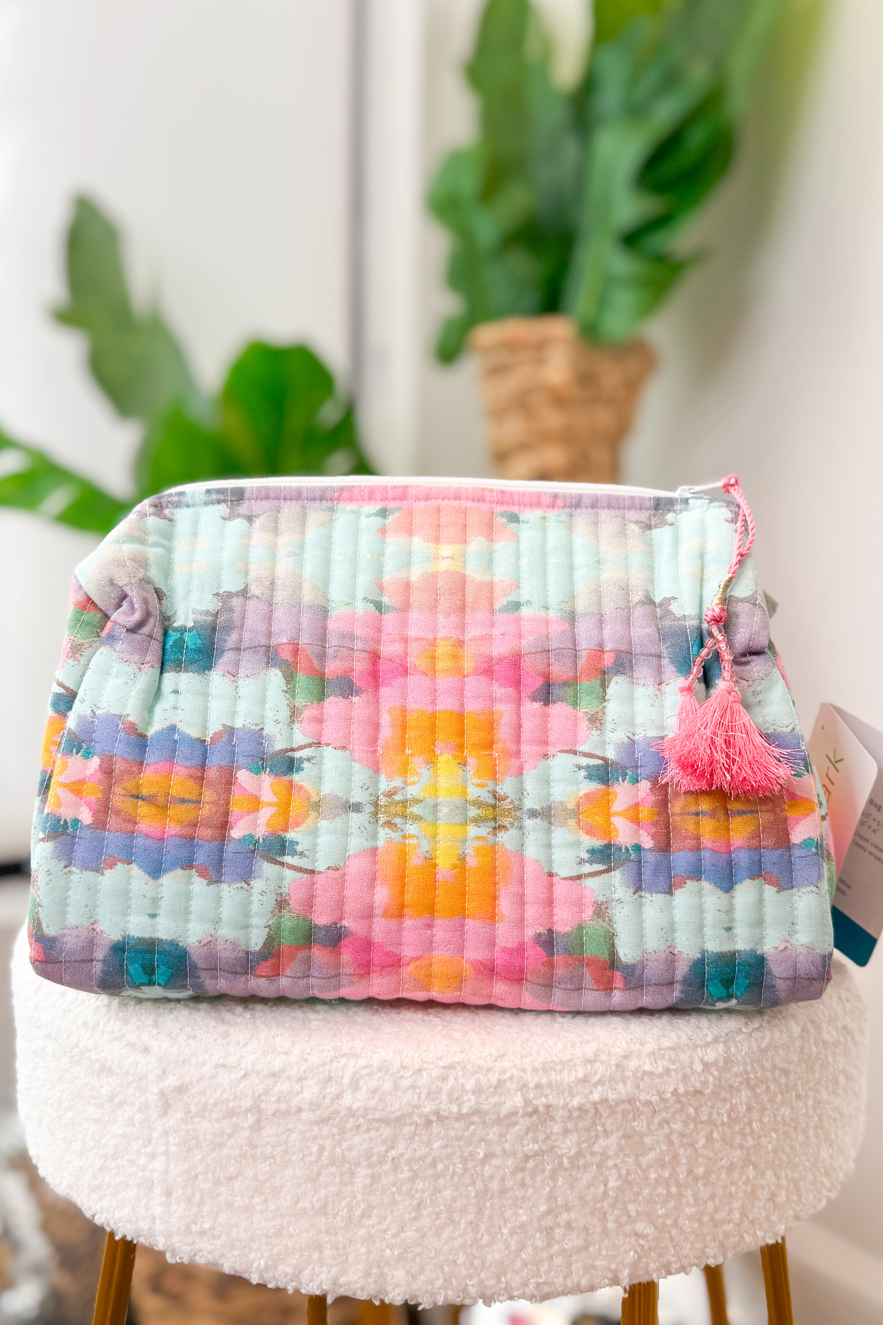 Floral quilted pouch with a pink tassel on a white surface with plants in the background