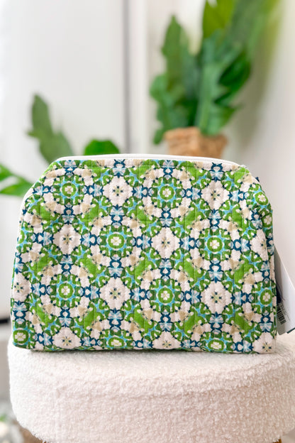 Cosmetic bag with green and blue pattern on a white surface with plants in the background