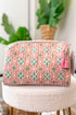 Floral patterned pouch with a pink tassel on a white surface with plants in the background