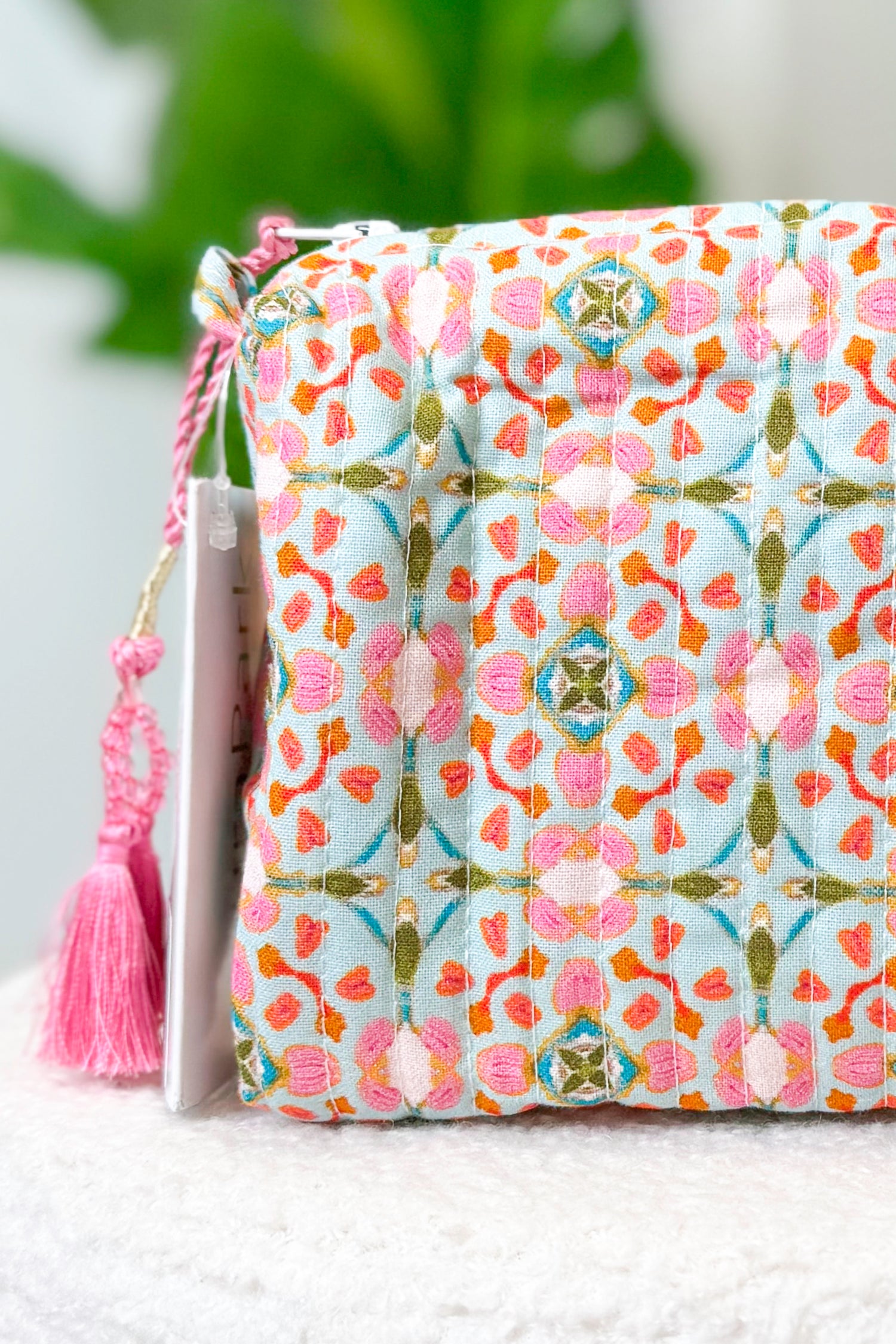 Fabric pouch with floral pattern and pink tassel on a white surface
