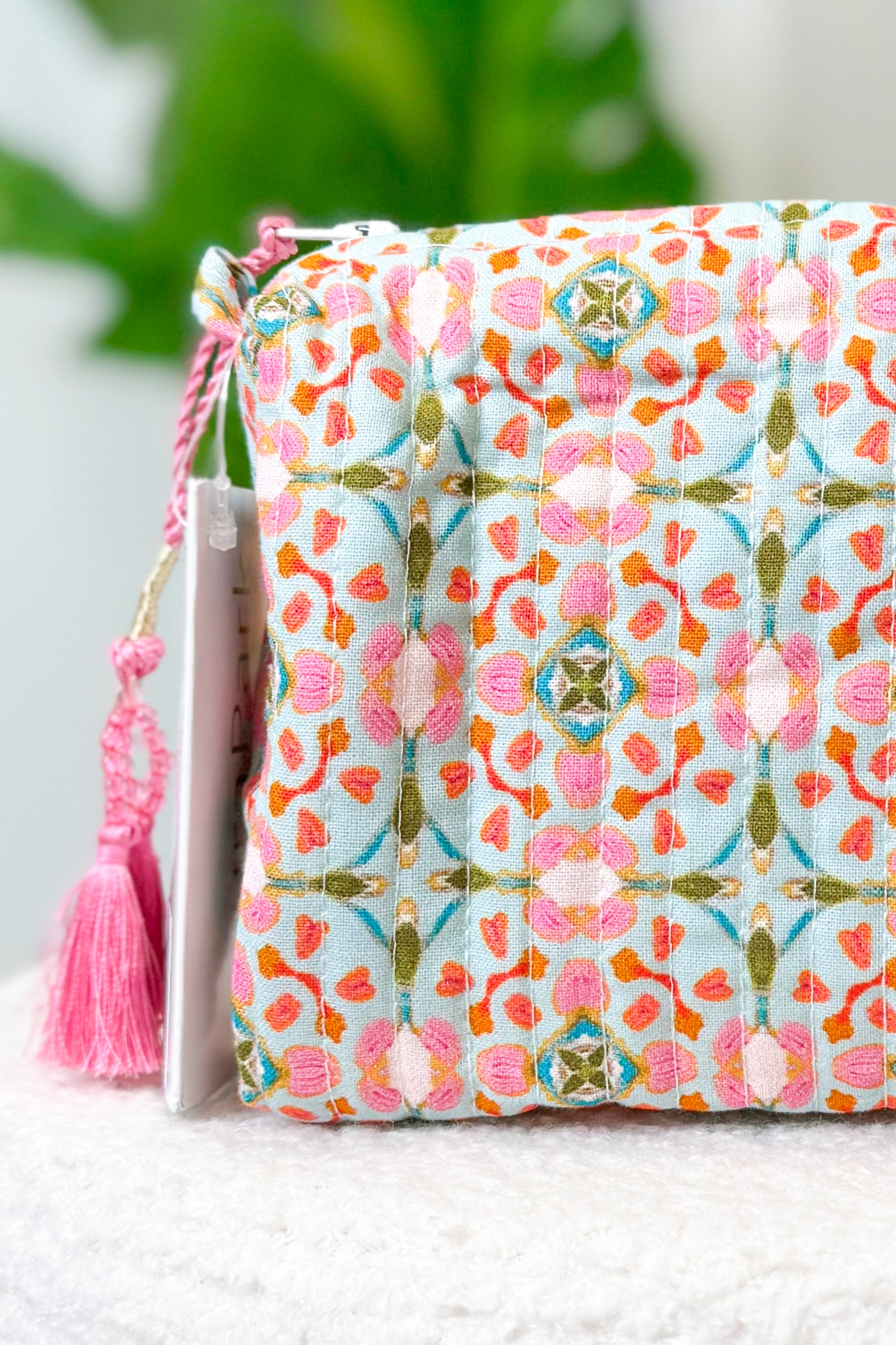 Fabric pouch with floral pattern and pink tassel on a white surface