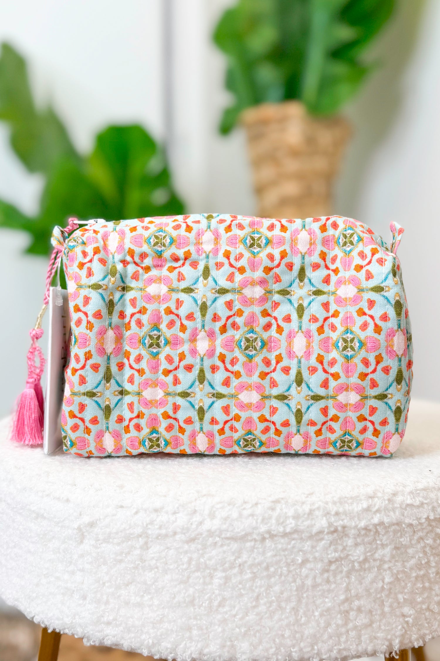 Floral patterned pouch with tassel on a white surface with plants in the background