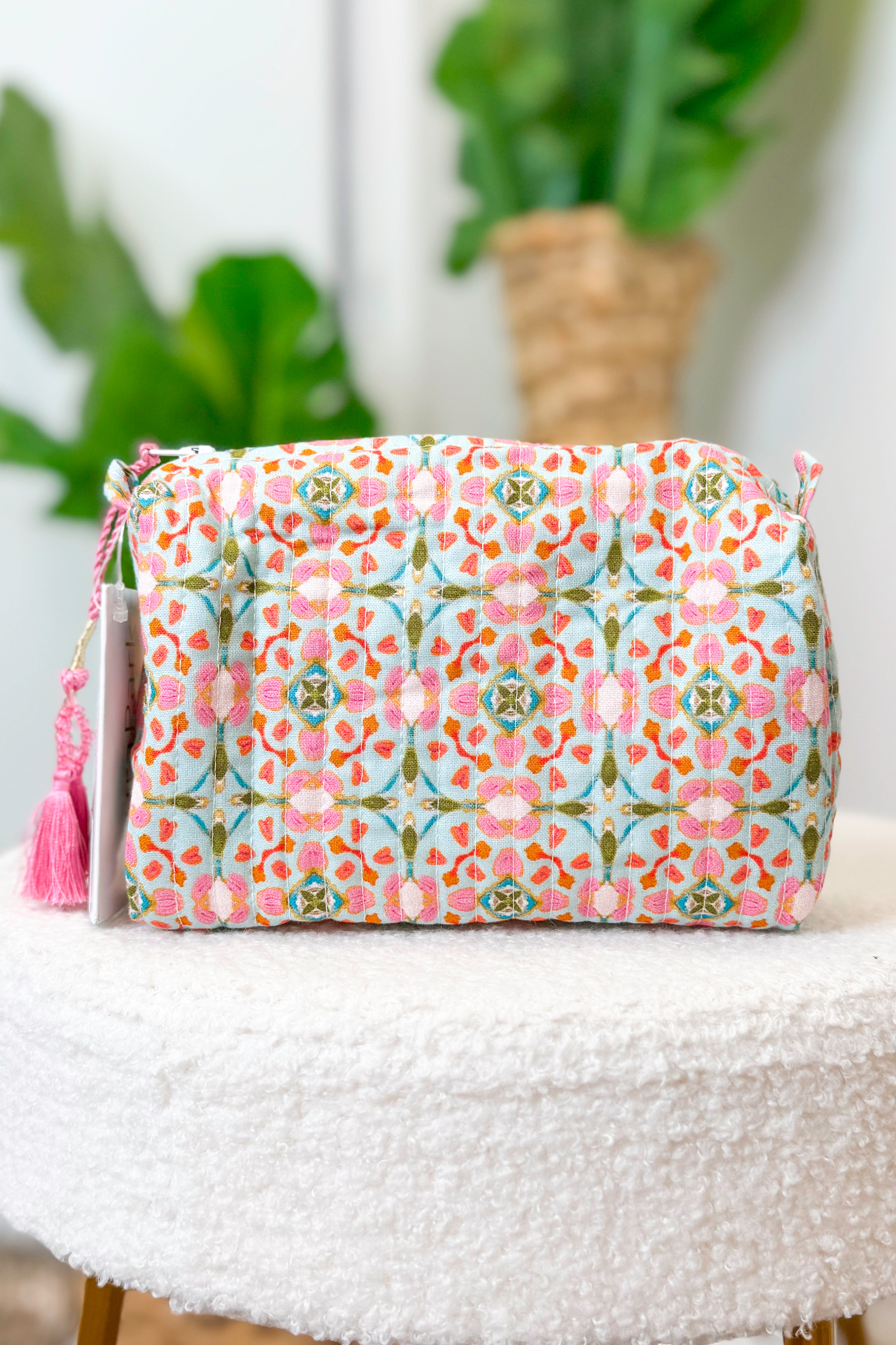 Floral patterned pouch with tassel on a white surface with plants in the background