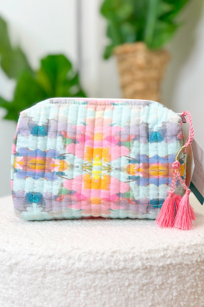 Multicolored woven pouch with tassels on a white surface with a blurred plant background