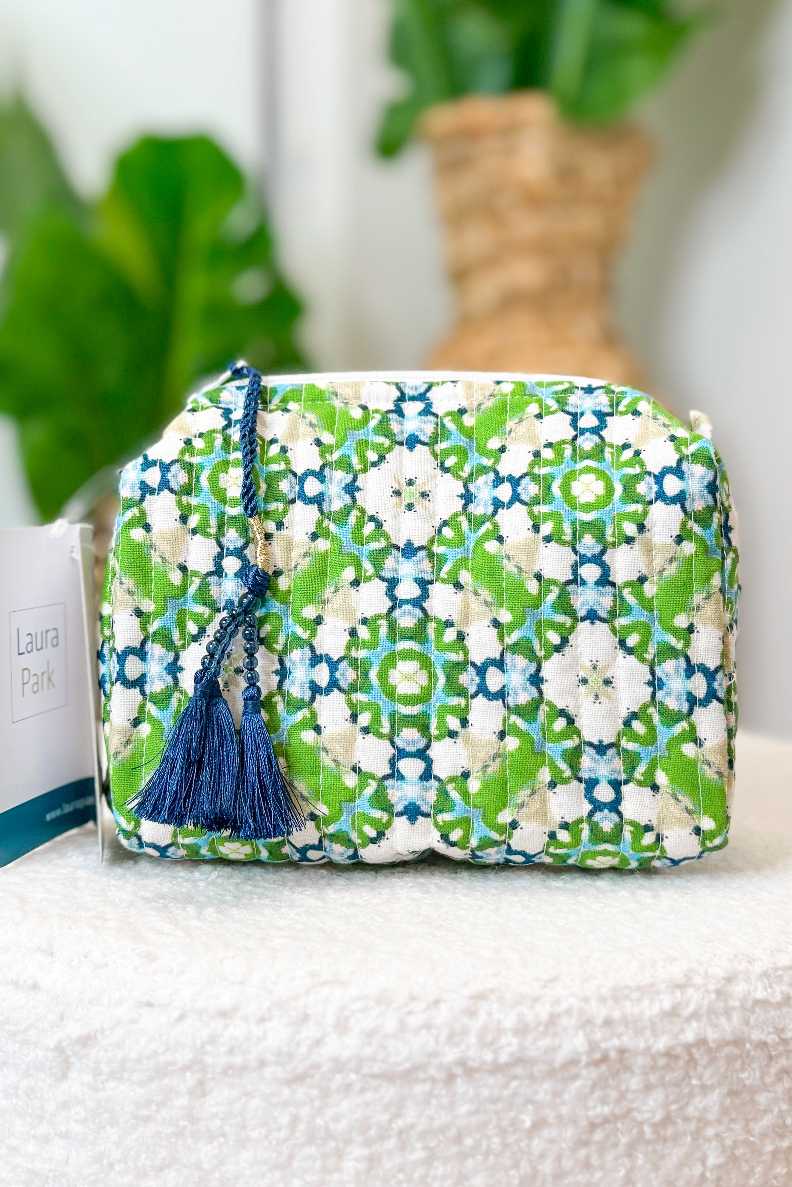 Patterned pouch with a tassel on a textured surface with plants in the background