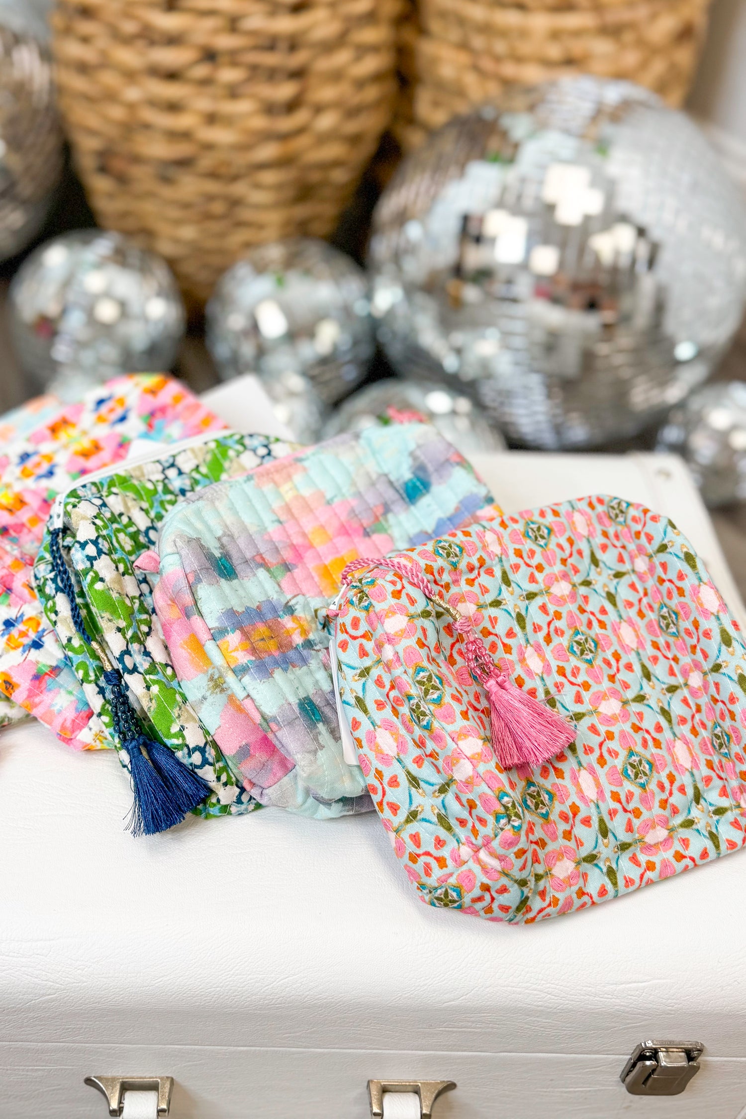 Decorative bags with floral patterns and tassels on a white surface with disco balls in the background.