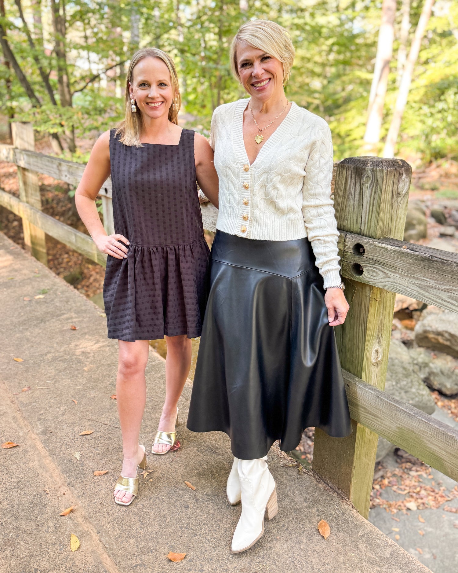 Two women standing outdoors by a wooden fence with trees in the background