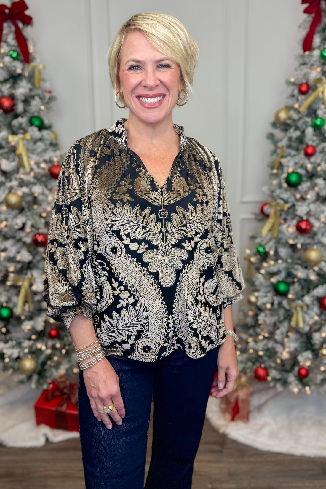 Front view of woman wearing Black With Velvet Pattern Top with jeans with holiday decor in the background.