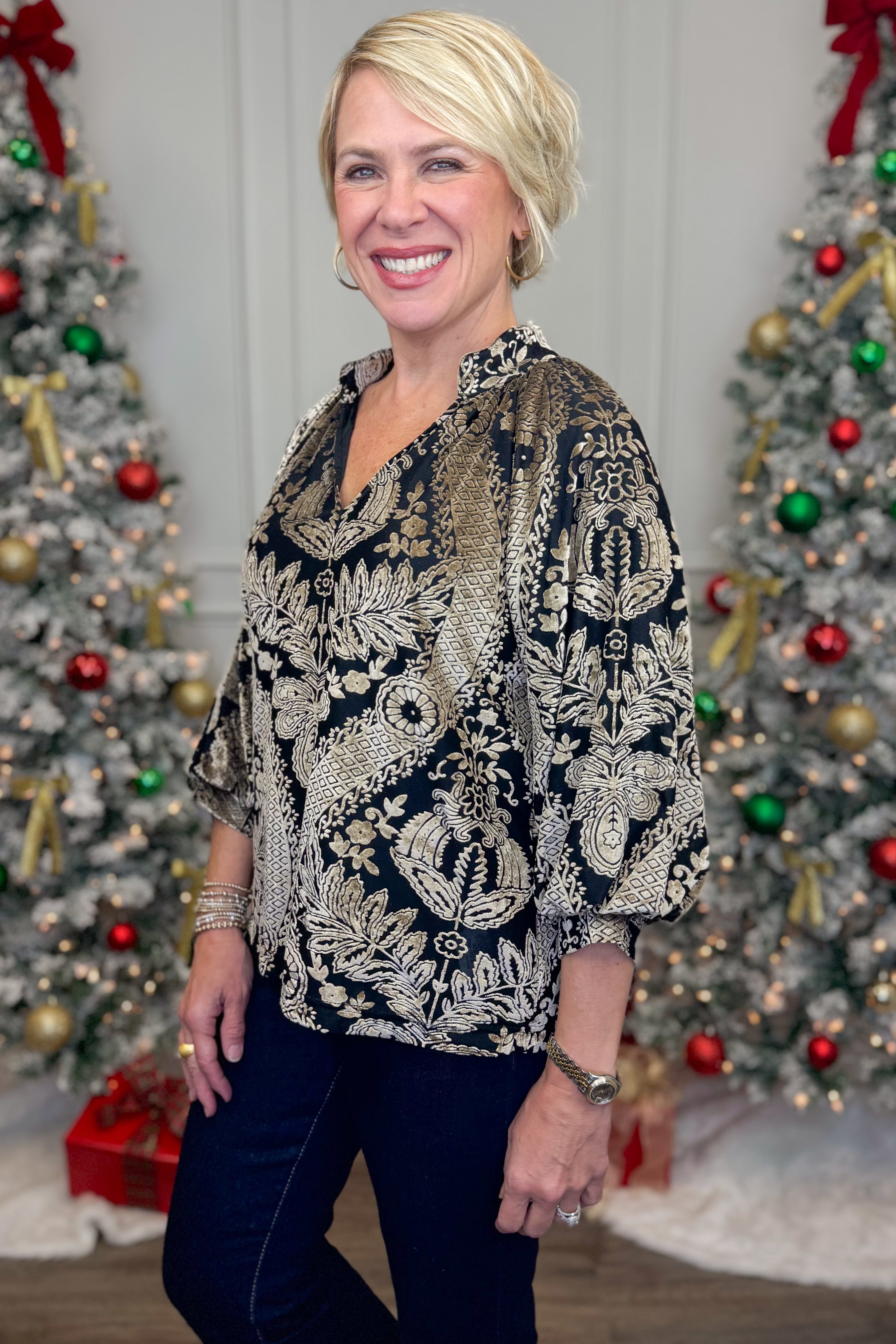 Side view of woman wearing Black With Velvet Pattern Top with jeans with holiday decor in the background.