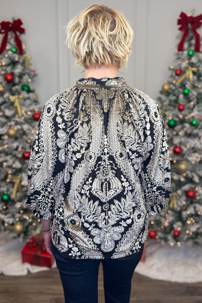 Back view of woman wearing Black With Velvet Pattern Top with jeans with holiday decor in the background.