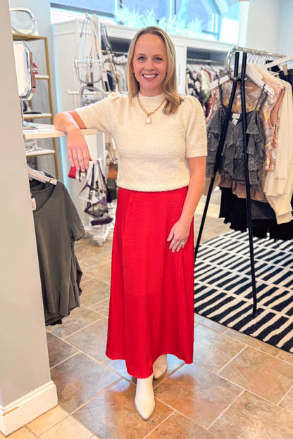 Front view of woman wearing cream top with Festive Red Northpointe Midi Skirt at a boutique.