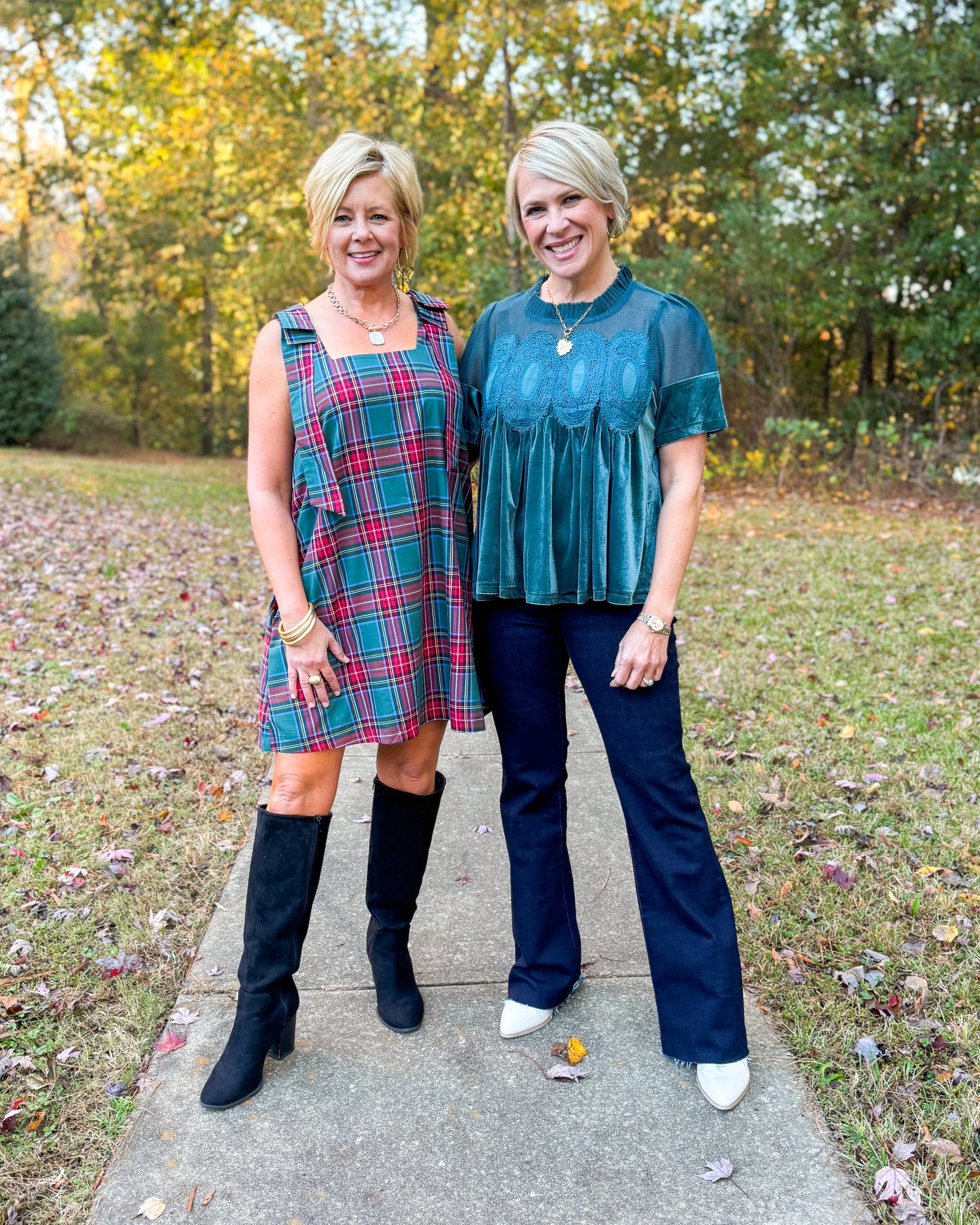 Two women standing on a sidewalk with trees and grass in the background