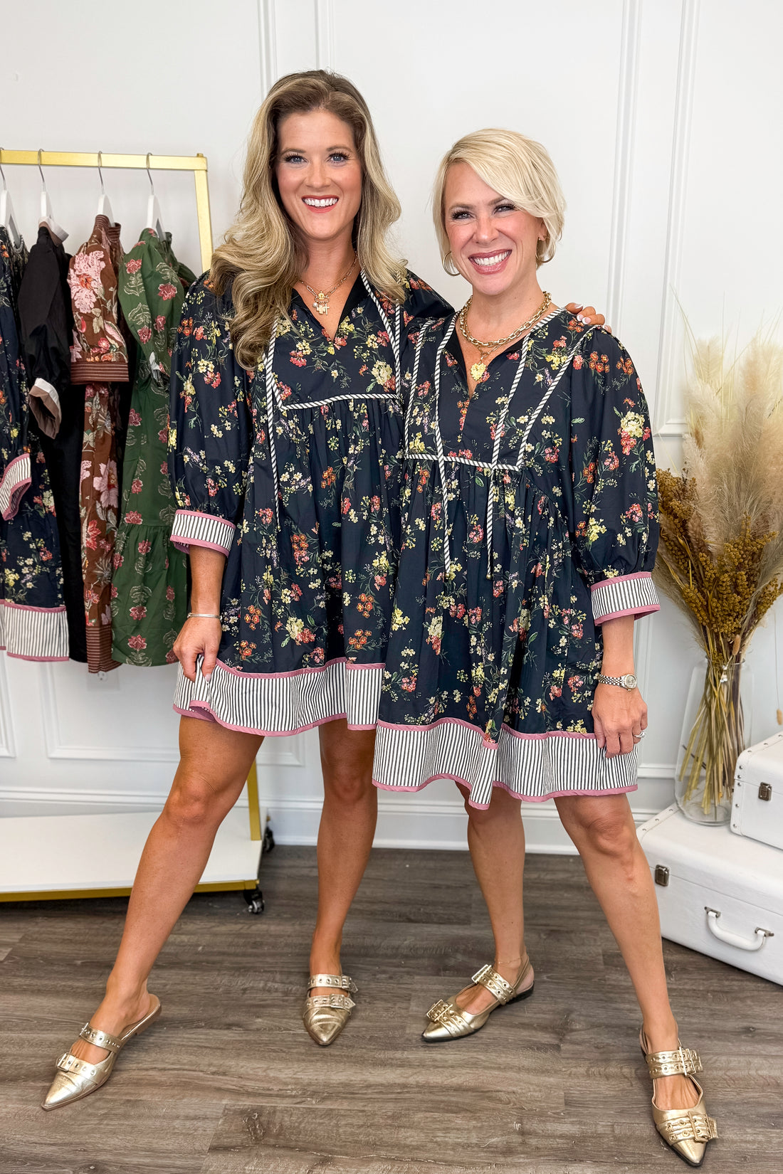 Two women wearing matching floral dresses in a clothing store.
