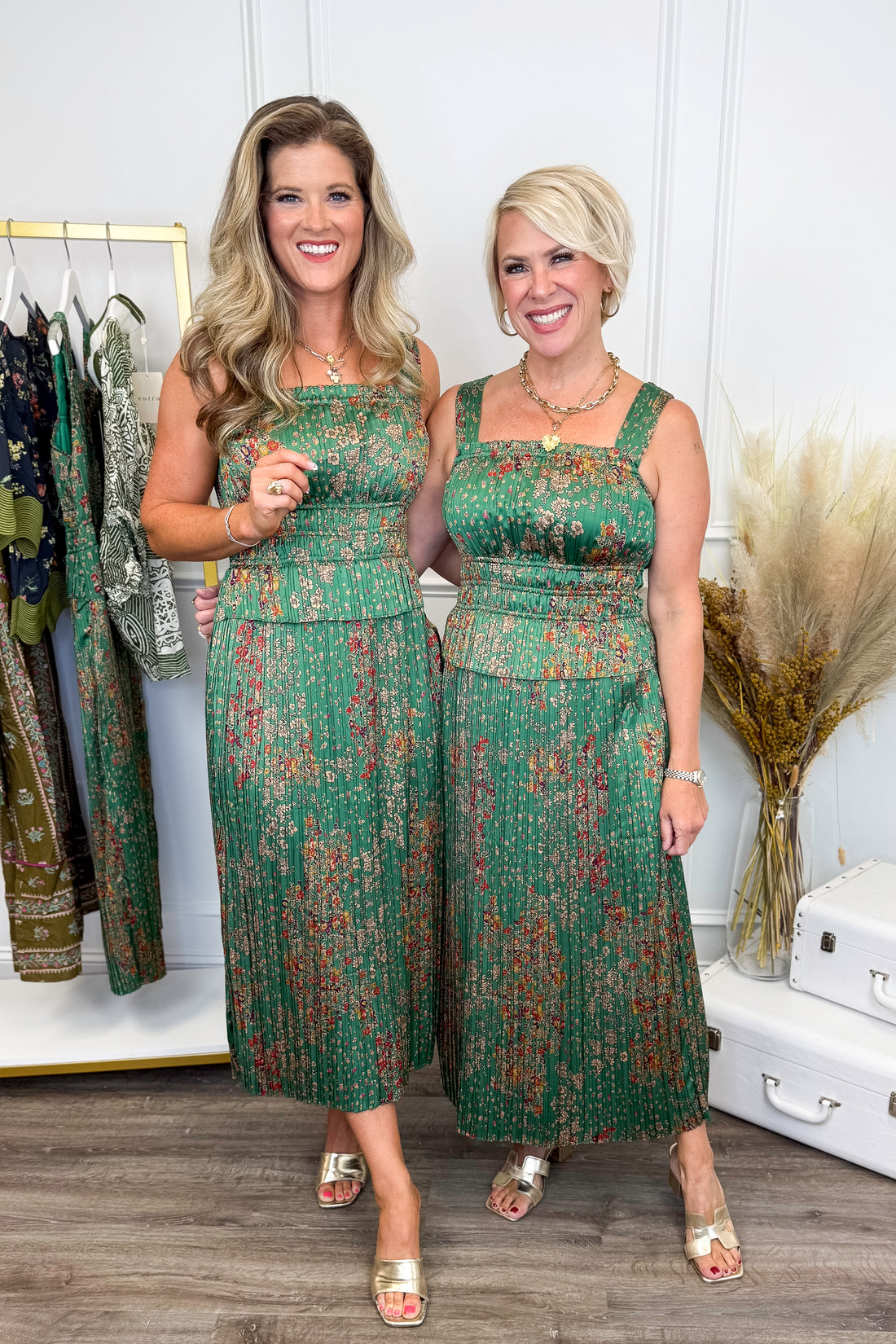 Two women wearing matching green patterned dresses in a clothing store.