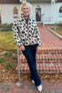 Woman wearing a leopard print jacket standing on steps outside a house.