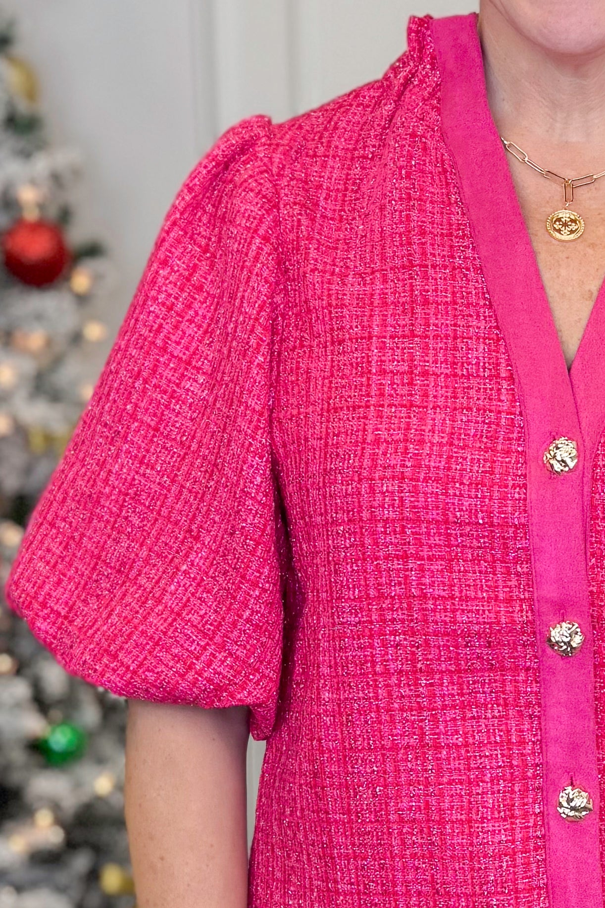 Woman in a pink jacket standing in front of Christmas trees with decorations.