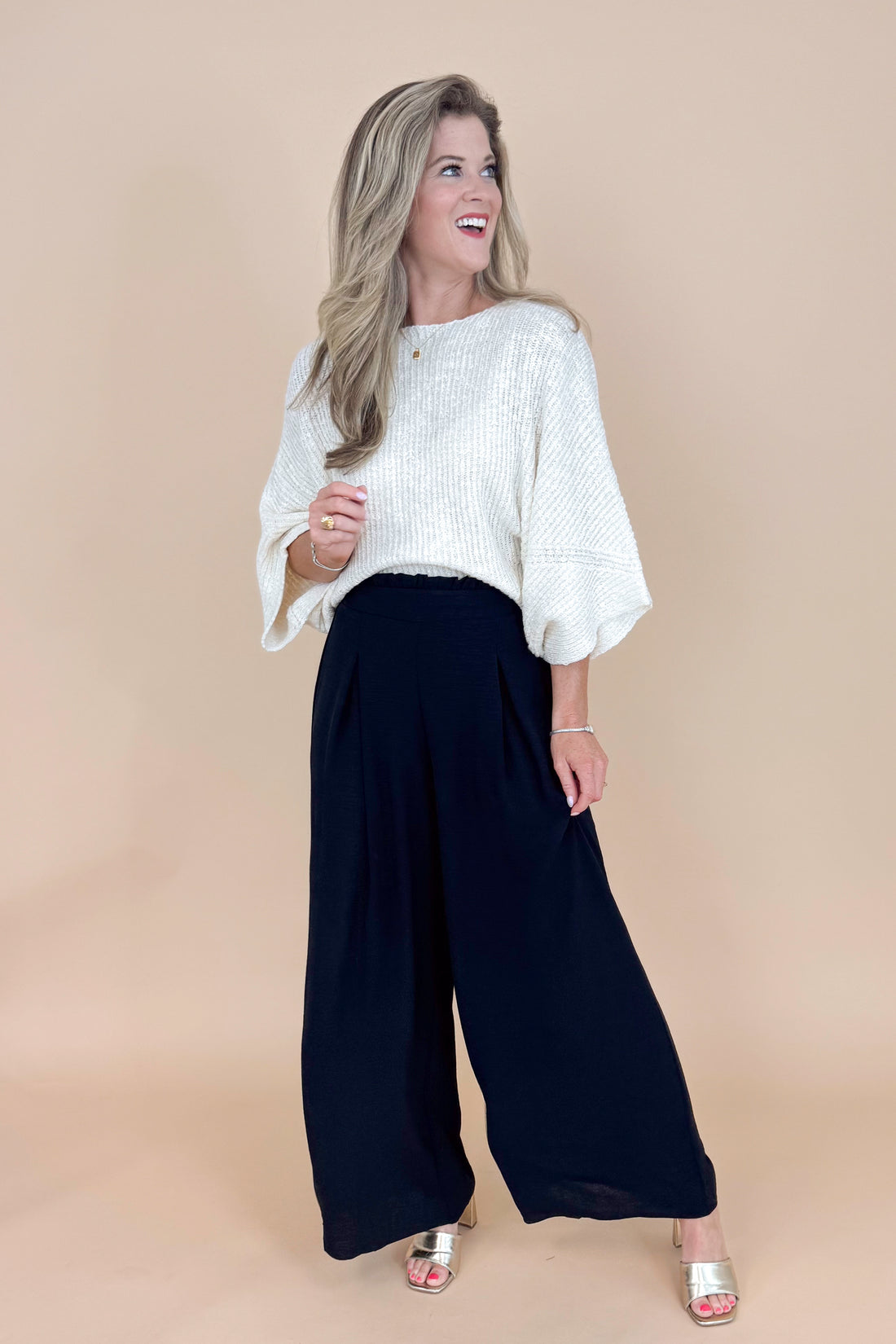 Woman wearing a white blouse and black wide-leg pants against a beige background