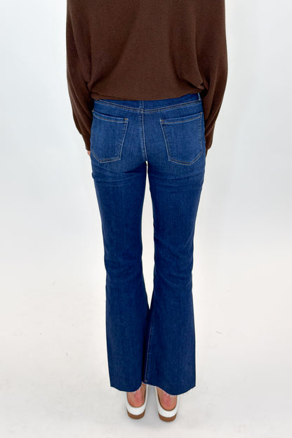 Back view of woman wearing Swagger Boutique’s Kelsey Ankle Flare Jeans In Dark Wash- Improve by Kut from the Kloth with brown top against white studio background.