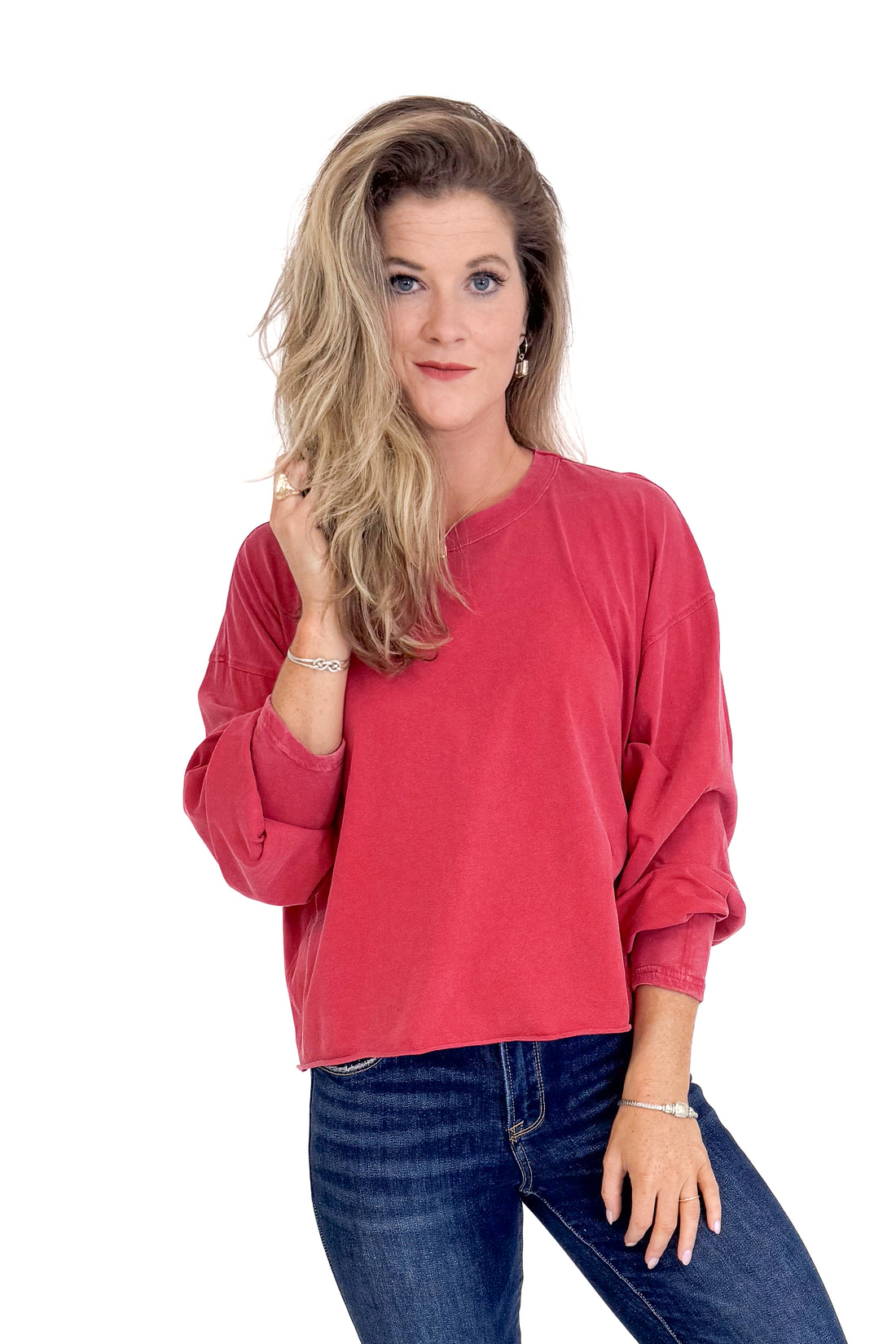 Woman wearing a red long-sleeve top and blue jeans on a white background