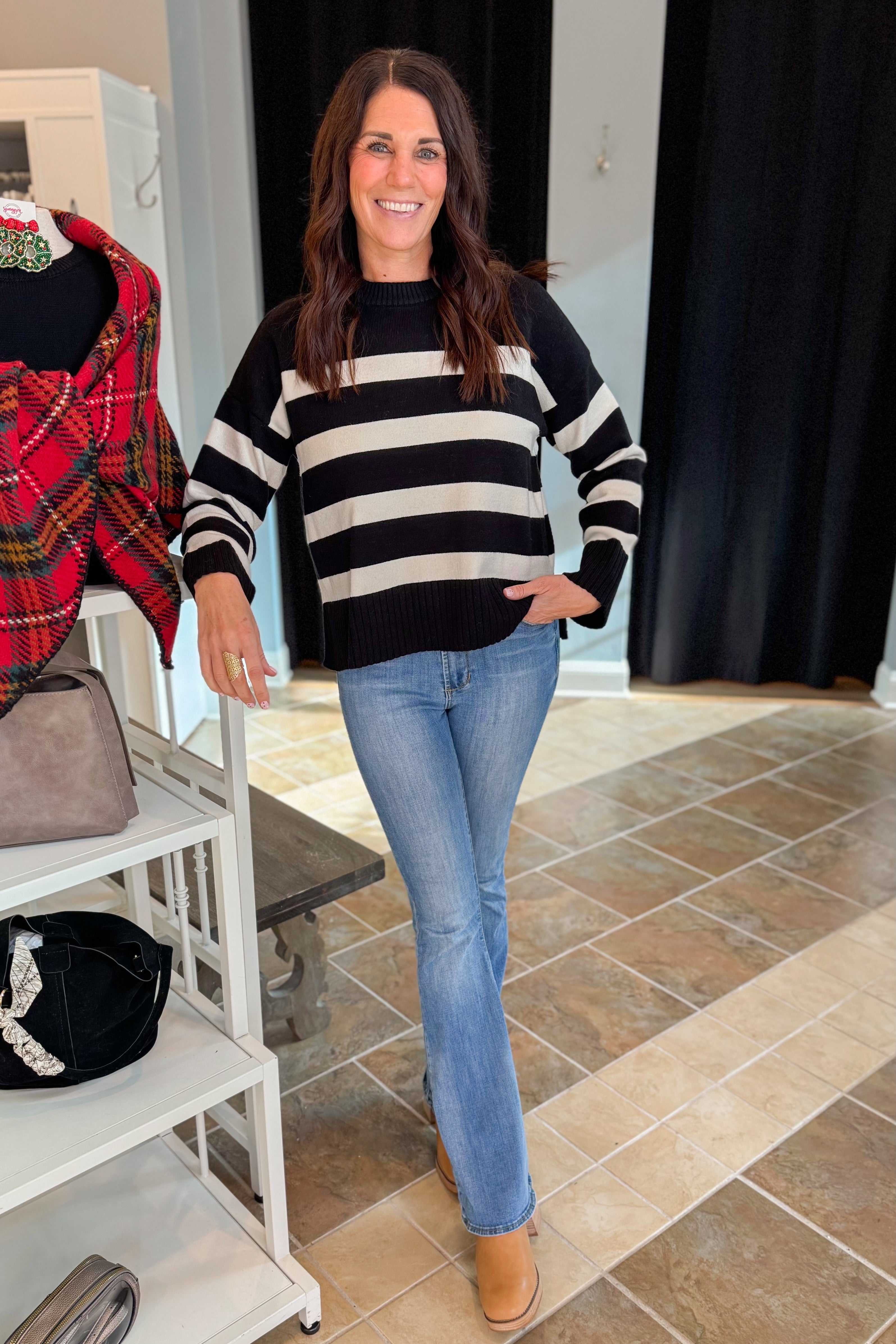 Front view of woman wearing Black and Cream Striped Crewneck Sweater with jeans at a boutique.